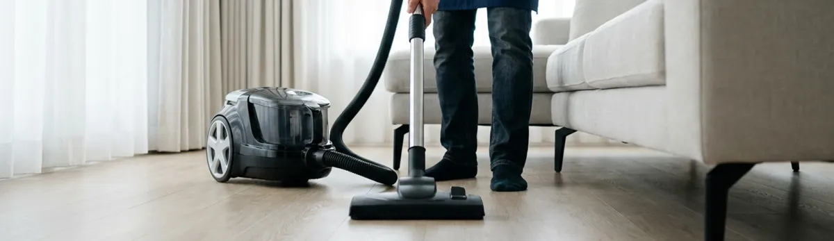 Professional house cleaner vacuuming a living room floor with a canister vacuum cleaner, Mobile, AL.