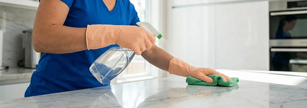 Maid service worker spraying and wiping a kitchen countertop with a microfiber cloth for sanitizing, Mobile, AL.